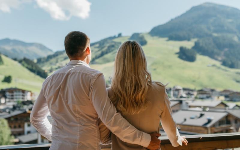 Paar auf dem Balkon des Hotels Alpine Palace mit Blick in den Ort
