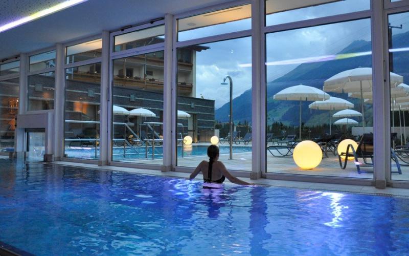 Eine Dame im Innenpool mit Blick auf den Aussenpool im Alpinhotel Jesacherhof bei Abendstimmung
