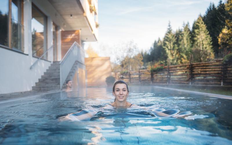 Eine Dame schwimmt im Aussenpool des Hotels GUT Trattlerhof und Chalets