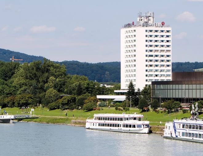 Aussenansicht des ARCOTEL Nike Linz Hotels mit der Donau im Vordergrund